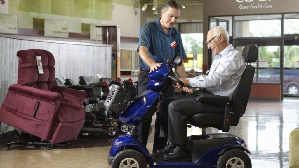 Image of person helping elderly man with a mobility scooter.