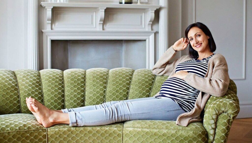 Image of pregnant woman on green couch, smiling.