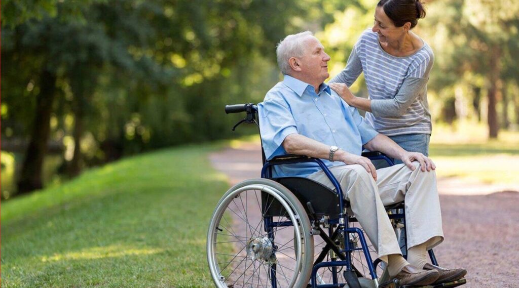 Image of person talking to elderly man in wheelchair.